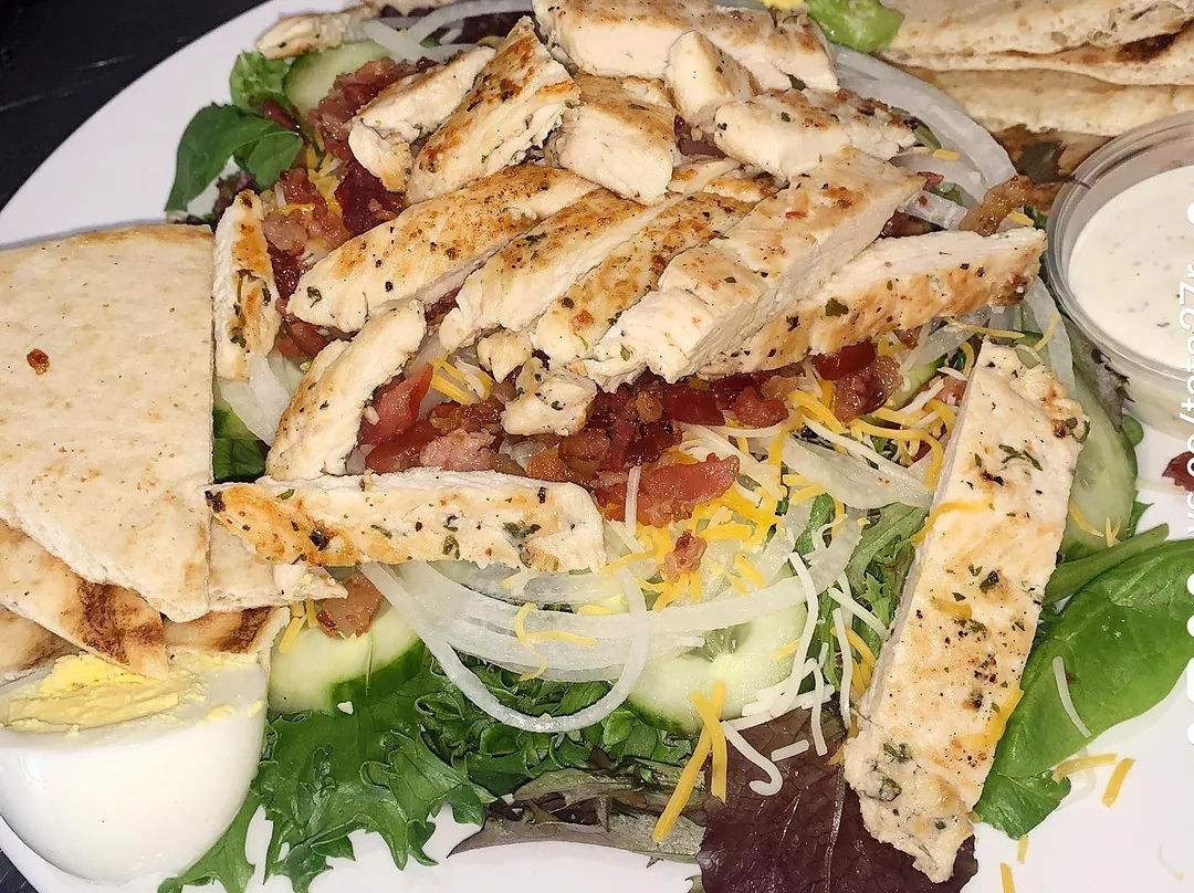 A big salad with grilled chicken, bacon, egg and pita
